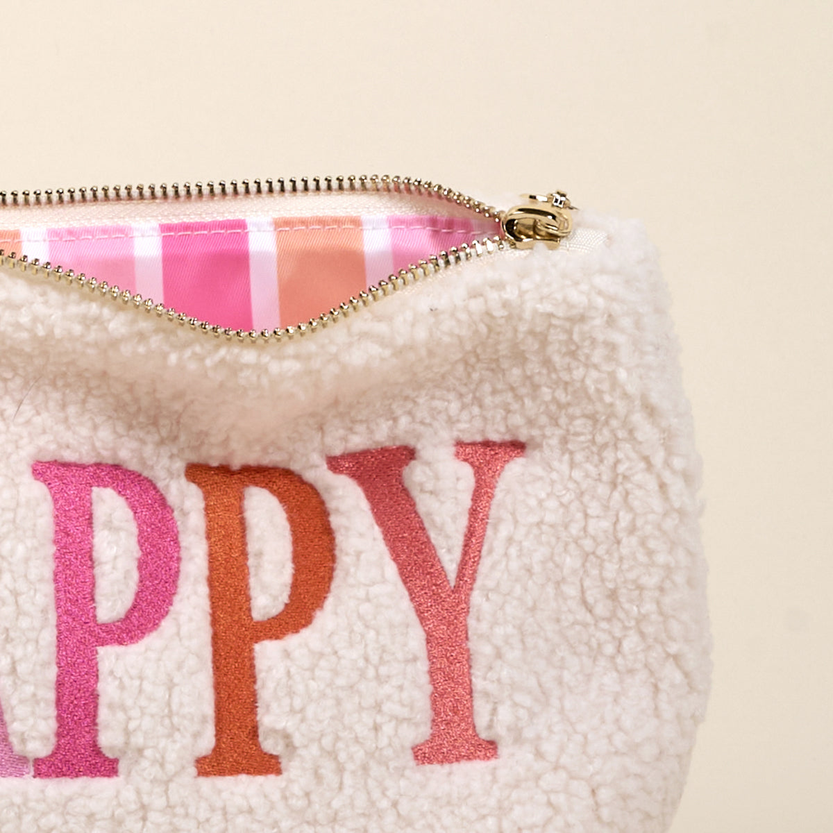 The Darling Effect’s Happy Edit Teddy Pouch features fluffy white sherpa with “HAPPY” embroidered in pink and orange, plus a striped pink-orange lining. A cute addition to your teddy pouch collection.