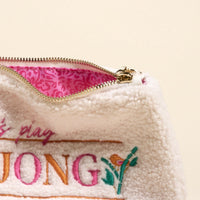 The Darling Effect Let's Play Mahjong Teddy Pouch features fuzzy cream sherpa, a gold-colored zipper, pink patterned lining, and embroidered "JONG" with floral detail and cursive text for a playful look.