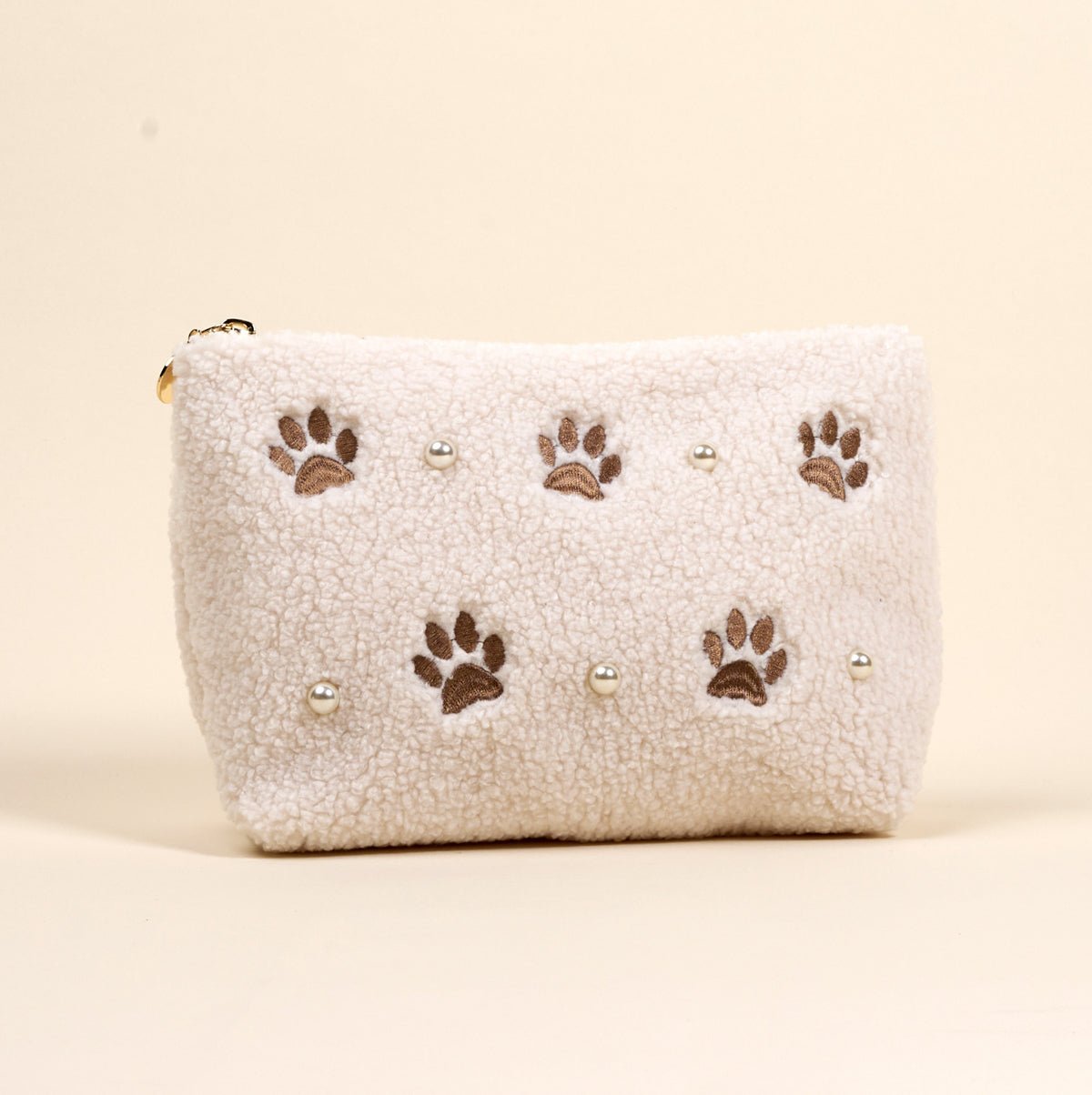 The Darling Effect’s Paws & Pearls Teddy Pouch is a fluffy white sherpa accessory featuring embroidered brown paw prints and pearl accents.