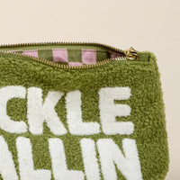 A close-up of the-darling-effect Pickleballin' Teddy Pouch shows its fuzzy green sherpa exterior with bold white lettering. The open zipper reveals a pink and green striped lining inside.