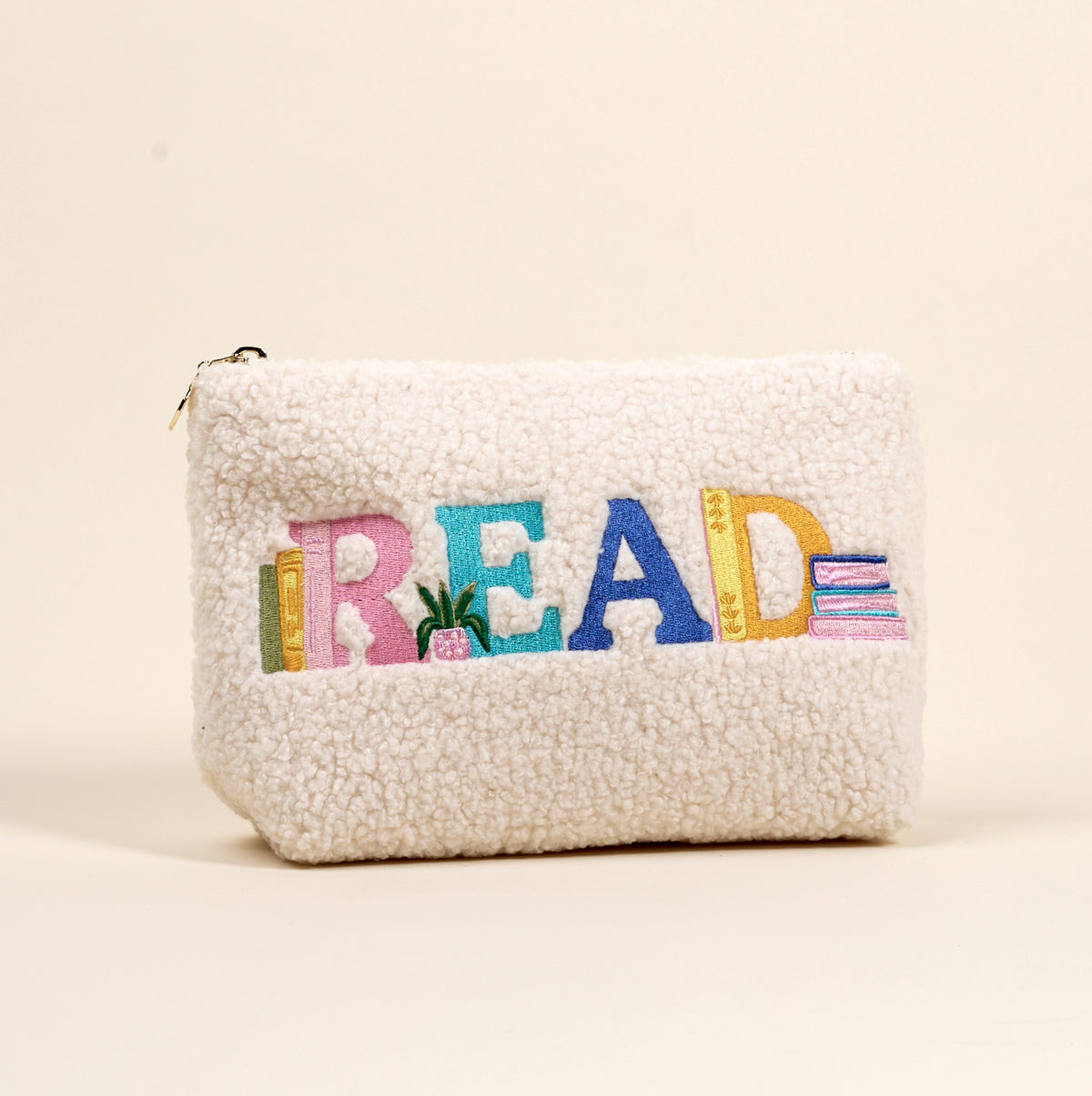 The Darling Effect’s Read Teddy Pouch features fluffy white sherpa, colorful “READ” embroidery, stacks of books, and a potted plant—perfect for on-the-go organization and teddy pouch lovers.