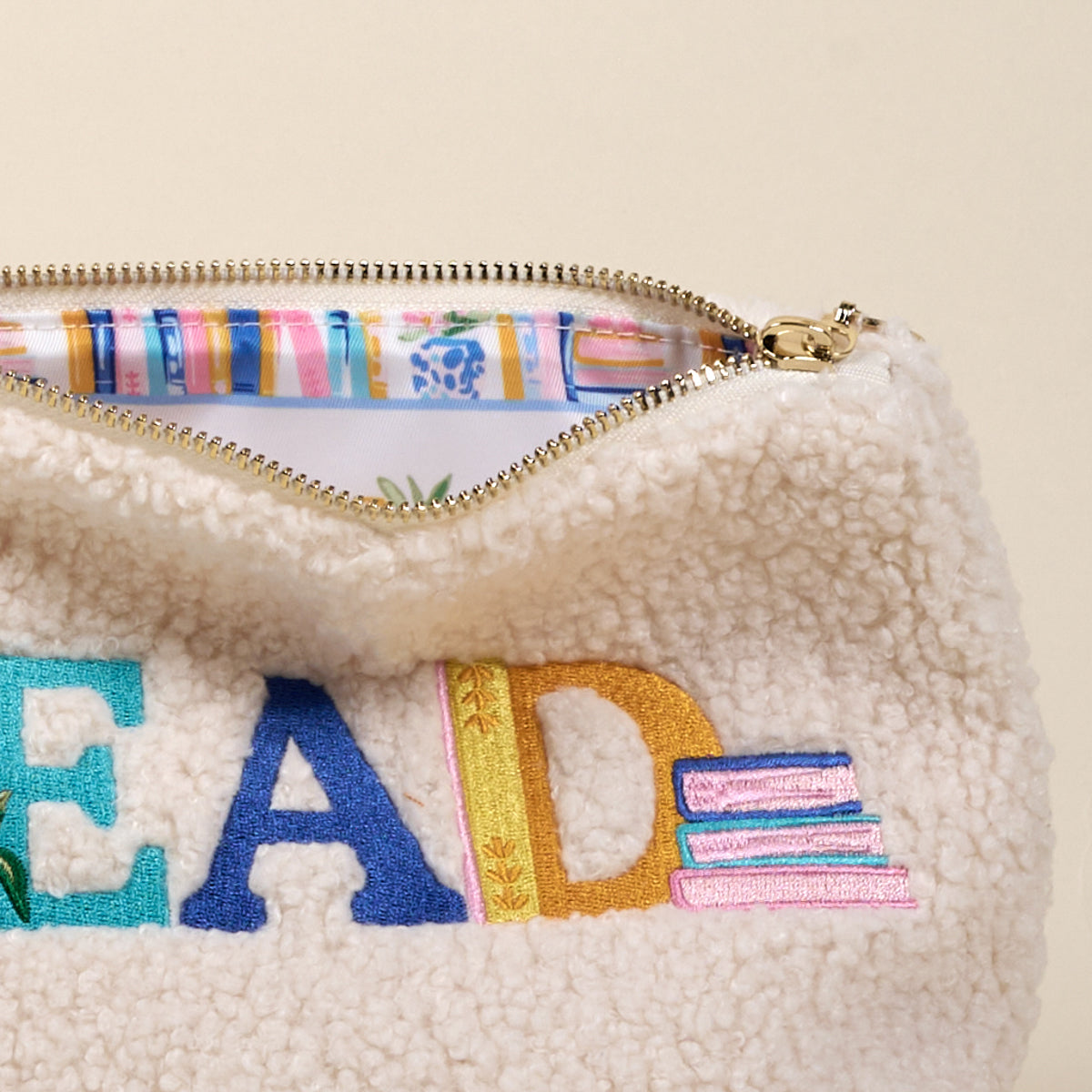 The Darling Effect’s Read Teddy Pouch is a cream sherpa bag with "READ" and books embroidered in colorful thread—perfect for organizing essentials or storing your favorite reads in cute, teddy-inspired style.