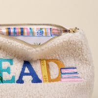 The Darling Effect’s Read Teddy Pouch is a cream sherpa bag with "READ" and books embroidered in colorful thread—perfect for organizing essentials or storing your favorite reads in cute, teddy-inspired style.