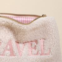 The Darling Effect’s Travel Edit Teddy Pouch is a cream sherpa pouch with pink "TRAVEL" embroidery and a gold zipper, perfect for adding cozy style to your accessories.