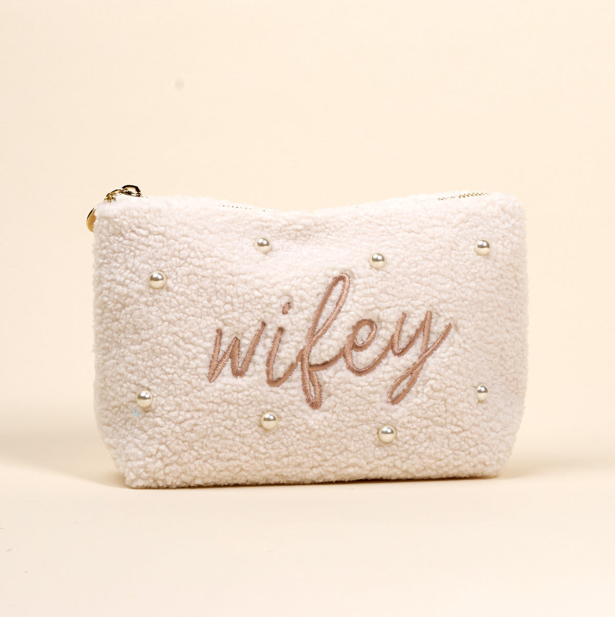 The Darling Effect Wifey & Pearls Teddy Pouch is a cream sherpa accessory, featuring embroidered "wifey" in script and scattered pearls—an adorable essential for any set.