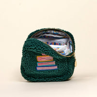 The Darling Effect’s Square Book Nook Teddy Pouch is small, green, and textured, with pastel books embroidered outside and a colorful book-themed lining inside.