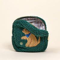 The Darling Effect’s Square Puppy Playtime Teddy Pouch is a green sherpa mini pouch with a gold zipper, plaid lining, an embroidered golden dog with blue bandana and tennis ball, plus a gold charm on the side.