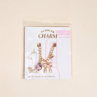 The Darling Effect’s Blushing Beauty Tumbler Charm set includes a gold chain with pink gem, bow, and heart charms, displayed on a white and pink card labeled “Tumbler Charm” and “ACCESSORIZE YOUR TUMBLER.”.