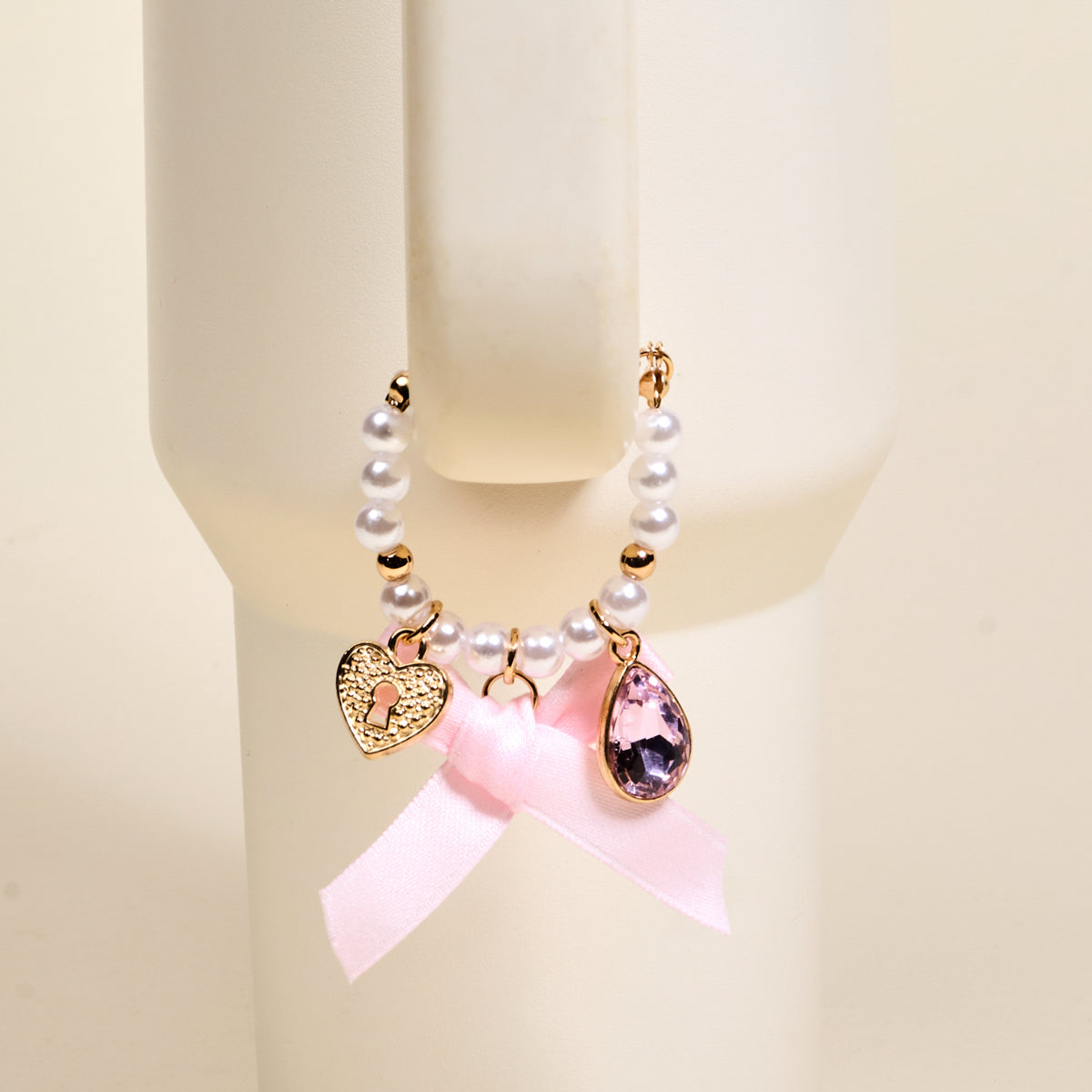 The Darling Effect Simply Coquette Tumbler Charm features white pearls, a gold heart lock, a pink teardrop gem, and a pink ribbon bow—perfect as a stylish tumbler accessory or unique drinkware charm.