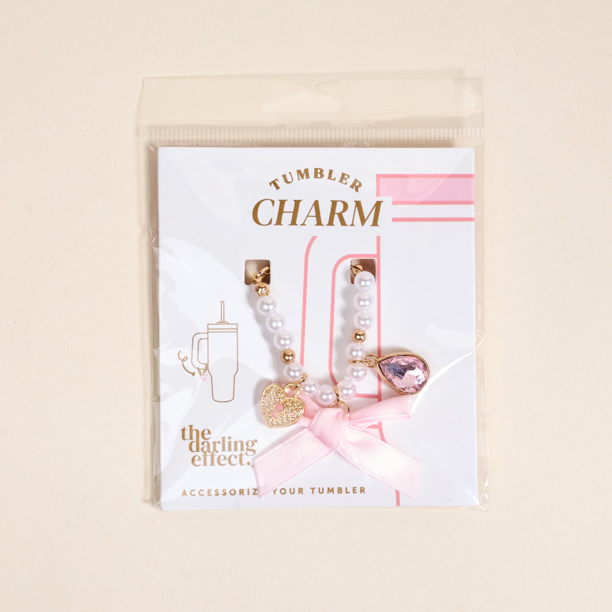 The Darling Effect Simply Coquette Tumbler Charm set features a strand of white beads with a pink bow, gold heart, and pink gem on a card labeled "Tumbler Charm"—a charming accessory for any drinkware charm lover.
