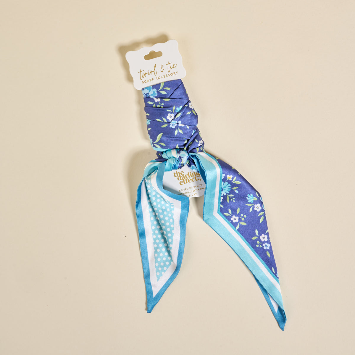 The Darling Effect's Endless Daydream Navy Twirl & Tie Scarf Accessory features blue floral fabric with polka dot trim, packaged on a white card. Style it endlessly for a versatile look.