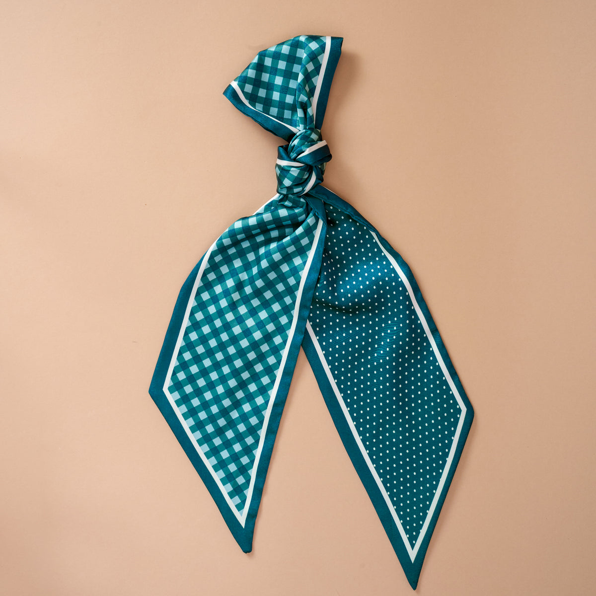 The Darling Effect's Gingham Green Twirl & Tie Scarf Accessory features a teal satin scarf with one side in a checkered pattern and the other in polka dots, stylishly tied in a loose knot and displayed against a light beige background—making it perfect for limitless styling possibilities.