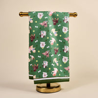 The Darling Effect's Dog Days Waffle Tea Towel, with cartoon dog faces, bones, and balls, is displayed on a gold stand against a beige background, bringing playful charm to any space.