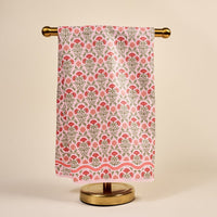 The Darling Effect's Everbloom Dusty Rose Waffle Tea Towel, featuring a red and orange floral pattern with green accents, hangs on a gold stand against a cream background.
