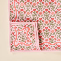 The Darling Effect's Everbloom Dusty Rose Waffle Tea Towel features a pink rectangular design with red, pink, and green floral patterns and stitched pink edges. One corner is folded to show the matching underside.