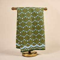 The Darling Effect’s Everbloom Forest Green Waffle Tea Towel features a blue and white floral block-print and wavy blue border, draped over a brass towel rack—an absorbent, stylish addition to any kitchen.