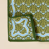 The Darling Effect Everbloom Forest Green Waffle Tea Towel features a floral print in white, blue, and yellow with a scalloped blue border and stitched dark green edging. One corner is folded to show the reverse side.