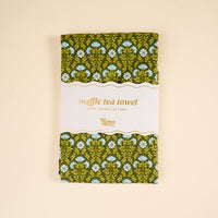 The Darling Effect’s Everbloom Forest Green Waffle Tea Towel features a dark green background with white and blue flowers and green leaves—a stylish, absorbent, and practical addition to any kitchen.