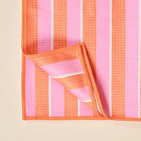 Close-up of The Darling Effect's Sicily Stripes Pink Waffle Tea Towel, featuring orange, pink, and white vertical stripes, absorbent textured surface, and orange stitched edges.