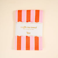 The Darling Effect's Sicily Stripes Pink Waffle Tea Towel features bold orange and pink vertical stripes on absorbent waffle-knit fabric, adding a stylish touch to any cream-background kitchen.