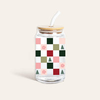 The Darling Effect Round Glass Cup - Holiday Check features clear Libbey glass with a bamboo lid and straw, adorned with a colorful checkered pattern of green, pink, and red squares along with small flowers and tree icons.